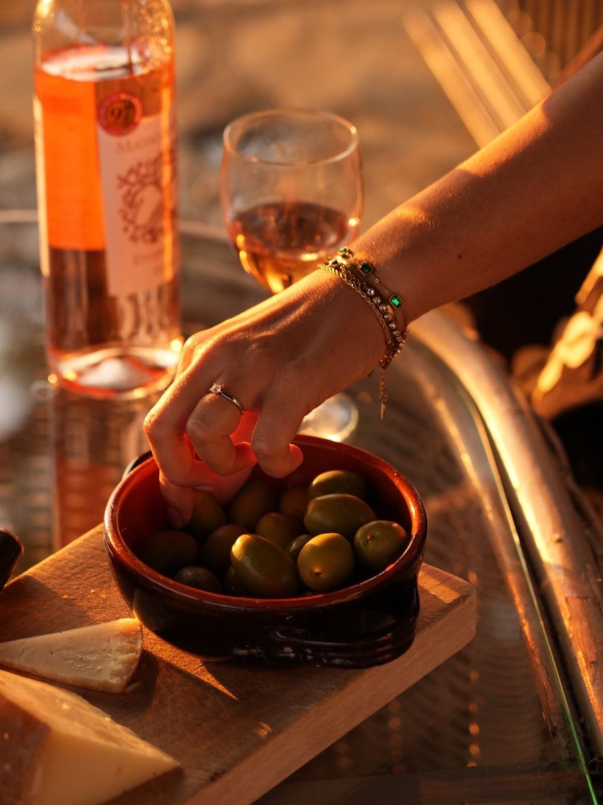 Mano tomando una aceituna de un cuenco de barro en una mesa iluminada por la última luz de la tarde