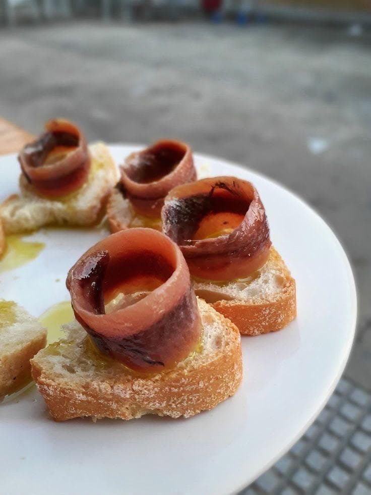 Pintxos de anchoa sobre pan tostado sobre un plato blanco, terraza exterior