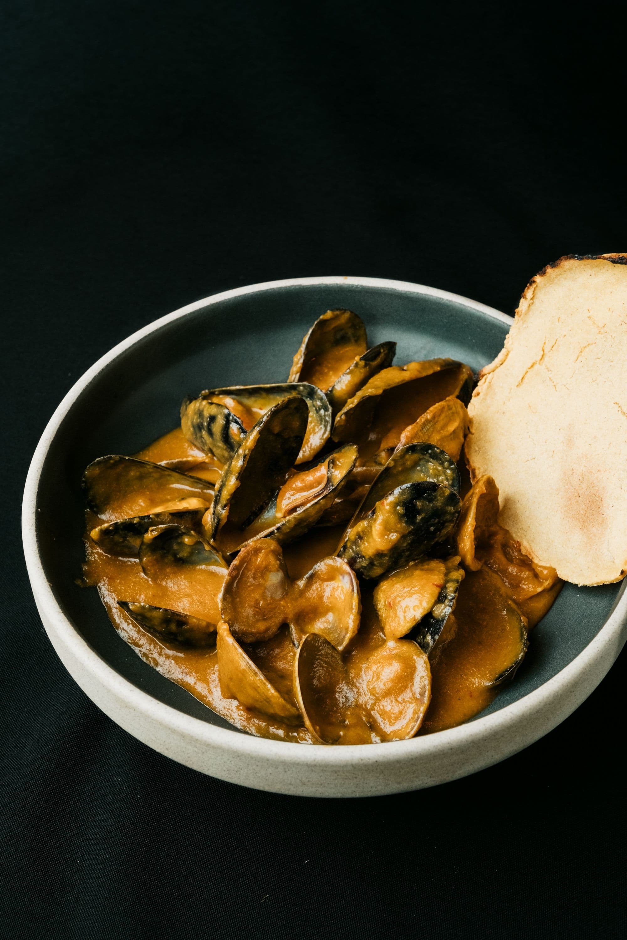 Mejillones en salsa servidos con pan sobre fondo oscuro
