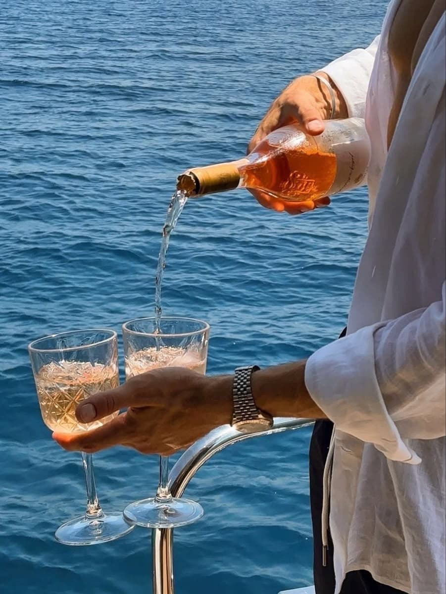 Vino rosado sirviéndose en copas de cristal, encuadre cercano a las manos y las copas