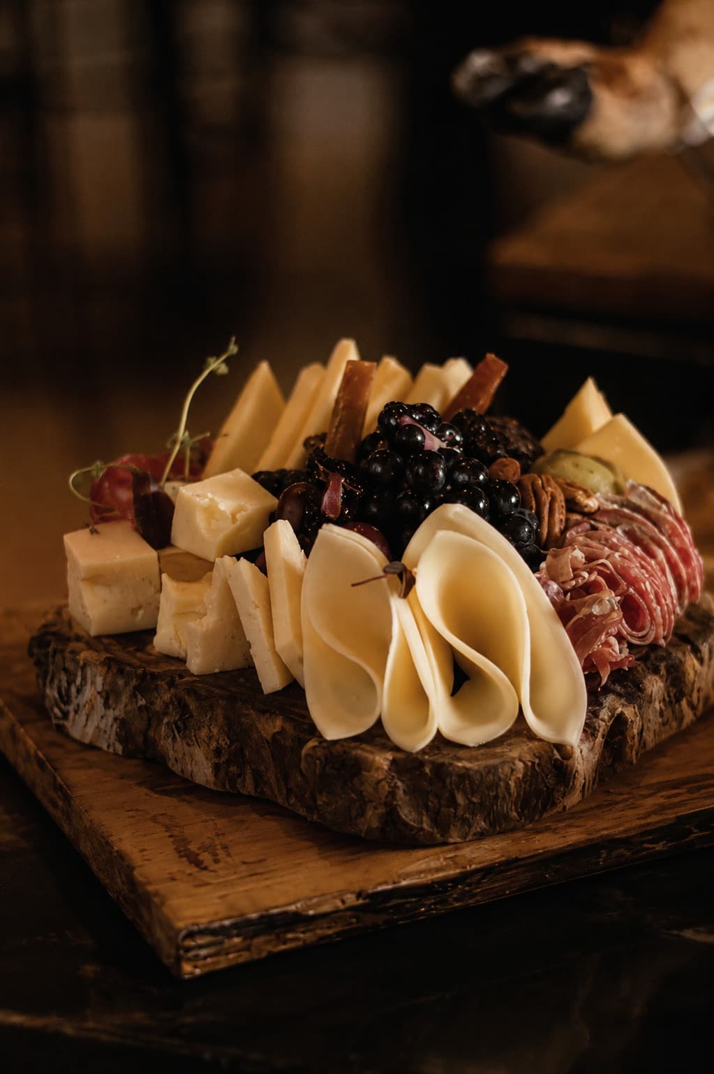 Tabla de quesos, embutido y uvas negras sobre tronco de madera