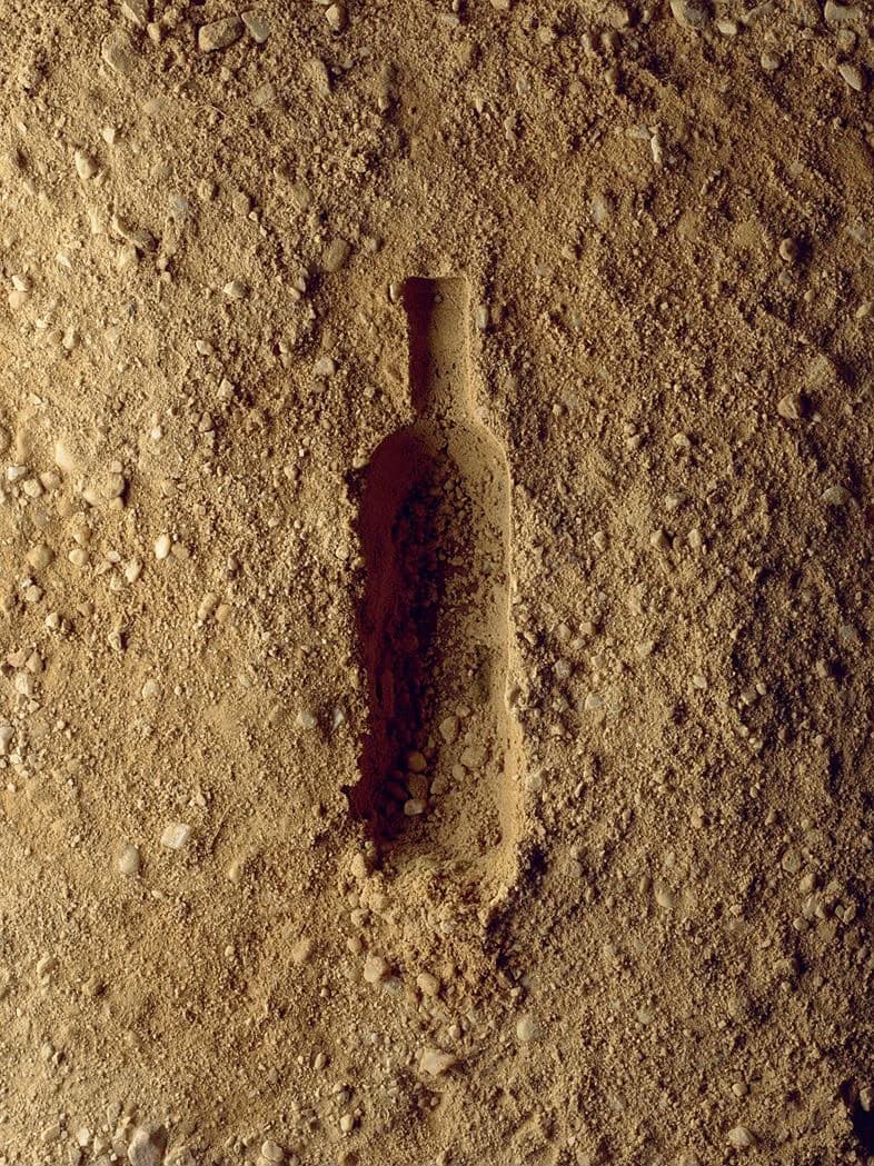 Silueta de una botella impresa sobre tierra seca y pedregosa, imagen conceptual de origen